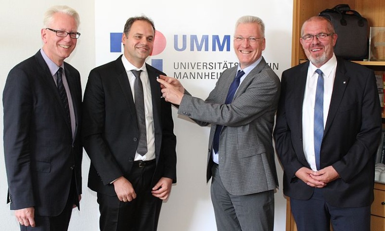 Prof. Hans-Jürgen Hennes (2.v.r) steckt Prof. Sascha Gravius (2.v.l.) die...